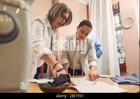 Ein kompetentes Team aus zwei Modedesignerinnen arbeitet an einer Kollektion von Nähmustern, um eine neue Kollektion stilvoller moderner Kleidung in einem Ta zu kreieren Stockfoto