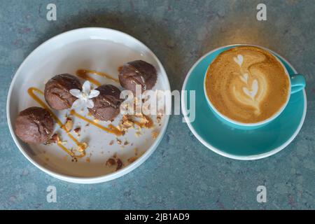 Draufsicht Coffee Latte in blauem Glas mit Bananencupcake auf weißem Teller. Ausgewählter Fokus. Pausenzeit-Konzept Stockfoto