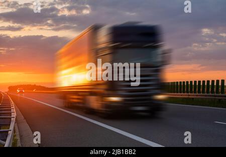 LKW auf der Autobahn während spektakulärer Sonnenuntergang, absichtliche Bewegungsunschärfe Stockfoto