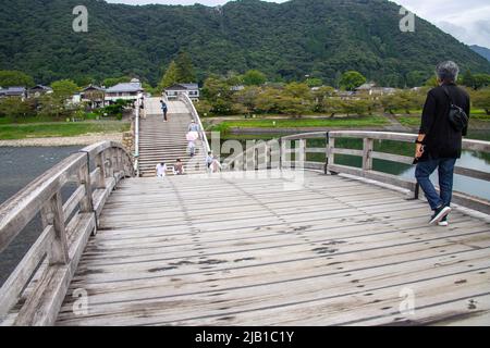 Touristen, die an bewölkten Tagen über die Kintai Bridge (Kintaikyo), eine historische Holzbogenbrücke, wandern. Es wurde 1673 erbaut und erstreckt sich über den Nishiki River Stockfoto