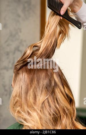 Professionelle Haarpflege. Junge weibliche Blondine mit langen Haaren, die in einem Schönheitssalon ein Haar stylen Stockfoto