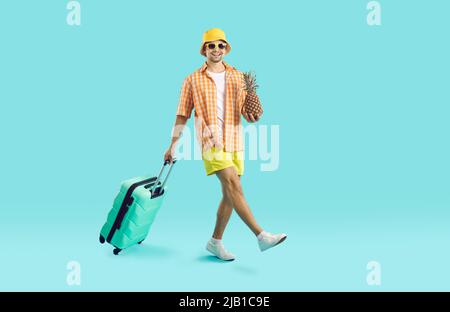 Fröhlicher, glücklicher junger Mann mit Koffer und Ananas wird in den Sommerferien fliegen. Stockfoto