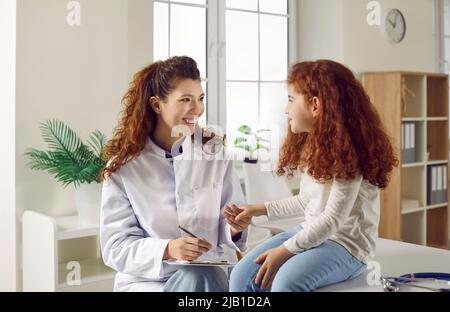 Freundliche Kinderärztin hält die Hand des kleinen Mädchens und spricht mit ihr während der ärztlichen Untersuchung. Stockfoto