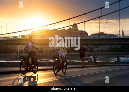 Die Menschen radeln und joggen am Fluss in einer Stadt, Sonnenuntergang Tine Stockfoto