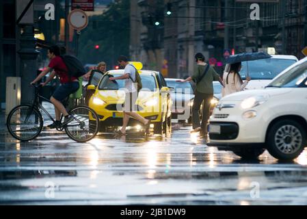 Niederschlag in der Stadt. Menschen überqueren die Straße und springen über Pfützen Stockfoto