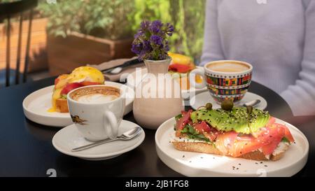 Wunderschön dekorierter Toast mit Lachs und Avocado, Ei benedict und Cappuccino das Frühstück ist die Tageszeit für Meetings Stockfoto