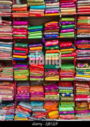 Schicke indische Sarees, fein säuberlich gestapelte bunte Seidensaris in Regalen in einem Textilgeschäft. Unglaubliches Indien. Stockfoto