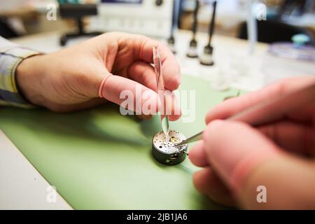 Nahaufnahme eines nicht erkennbaren Mannes in Gummihandschuhen mit einer Pinzette, während Quarzflüssigkeit in das Uhrwerk gegeben wird Stockfoto