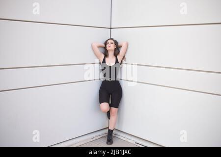 Ganzer Körper einer jungen Frau in schwarzem Anzug und Schuhen, die die Kamera anschaut, während sie in einer modischen Pose steht Stockfoto
