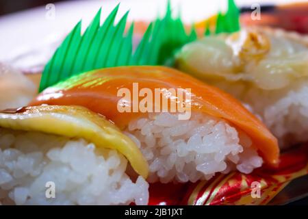 Lachs-Sushi aus der Nähe mit Anago-Sushi (Conger Aal) und Kai (Shellfish) in einer Sushi-Packung zum Mitnehmen. Stockfoto