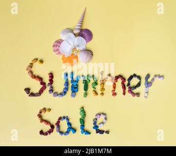 Inschrift Sommerverkauf aus bunten Seekieseln und Muscheln auf einem gelben Hintergrund. Saison der Sommer Rabatte, Business-Angebot für Käufer Stockfoto