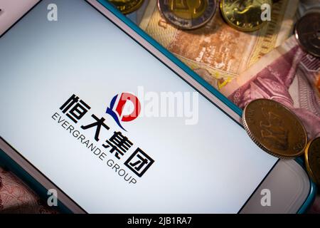 Kumamoto, JAPAN - Sep 23 2021 : die Evergrande Group, Chinas führender größter Immobilienentwickler, auf dem iPhone mit Zufallsmünzen und Banknoten Stockfoto