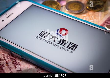 Kumamoto, JAPAN - Sep 23 2021 : die Evergrande Group, Chinas führender größter Immobilienentwickler, auf dem iPhone mit Zufallsmünzen und Banknoten Stockfoto