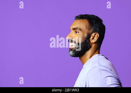 Profil-Headshot eines gutaussehenden, lächelnden afroamerikanischen Mannes mit Bart und purpurem Schnurrbart, der auf das Copy Space Studio blickt Stockfoto