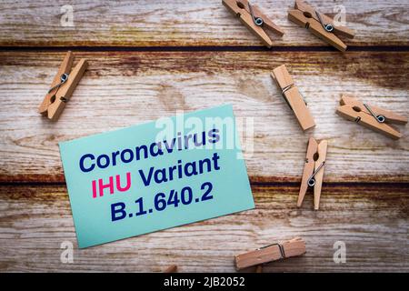 Nachrichtenkarte mit Coronavirus IHU Variante B.1.640.2 mit Holzkneife auf schäbigen schicken Tisch. Neue COVID-19-Variante in Südfrankreich nachgewiesen Stockfoto