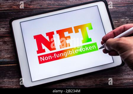 Ein Gradientenzeichen für NFT (Ein nicht-fungibler Token), eine nicht austauschbare Dateneinheit, die auf einer Blockchain auf einem Tablet gespeichert ist. Mann Hand hält einen Stylus-Stift Stockfoto