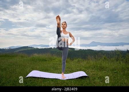 Kaukasisch fit Frau trägt Sport-BH und Leggings tun Fitness-Übungen auf Yoga-Matte im Freien. Freizeit zum Training in der Natur. Stockfoto