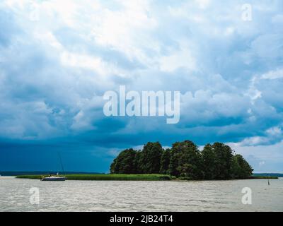 Einsame Insel und festgemacht kleine Segelyacht auf einem See und dramatische bewölkten Himmel auf dem Hintergrund Stockfoto