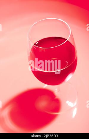 Ein Glas Wein mit dunklem Schatten. Weinglas in rot einfarbig. Stockfoto