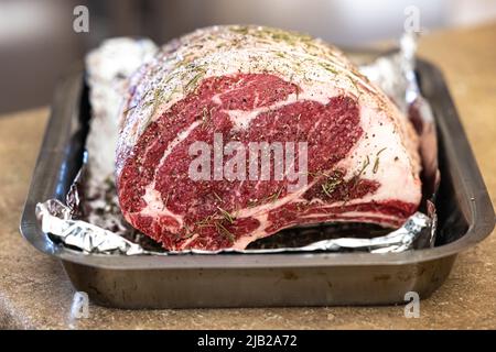 Roher Rippenbraten, gewürzt und auf einer mit Aluminiumfolie gefütterten Pfanne sitzend, bereit für den Ofen für ein Weihnachtsessen Stockfoto