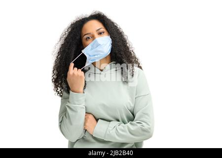 Glückliche multirassische Frau in formeller Kleidung, die ihre medizinische Maske auf Weiß isoliert auszieht. Nahaufnahme eines weiblichen Patienten, das sich vor einer Viruserkrankung schützt. Empfiehlt Maßnahmenkonzept Stockfoto