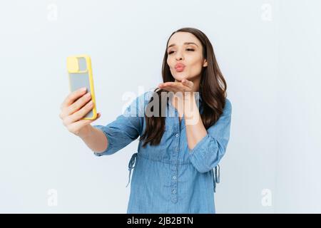 Porträt der jungen Brünette Frau, die Selfie und senden Luftkuss, weißen Studio-Hintergrund Stockfoto