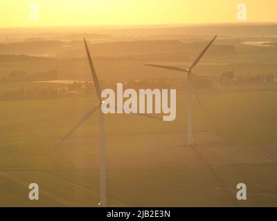 Aus der Vogelperspektive: Ackerland bei Sonnenuntergang in einer Reihe von Windturbinen, grüne Landwirtschaft und Dämmerung. Stockfoto