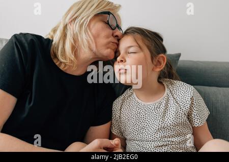 Reife Frau Großmutter küsst mit Liebe ihre Enkelin Vorschulkinder zu Hause auf dem Sofa Stockfoto