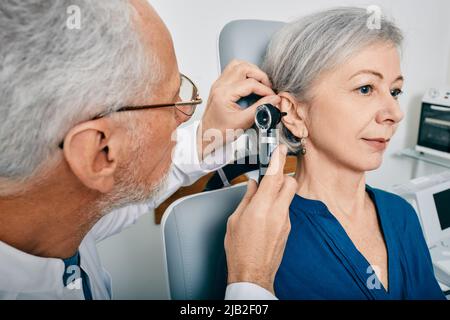 Der Arzt des Otolaryngologen überprüft das Ohr der älteren Frau mit einem Otoskop oder einem Ohrhörer in der medizinischen Einrichtung. Hörtest für ältere Menschen, Otoskopie Stockfoto
