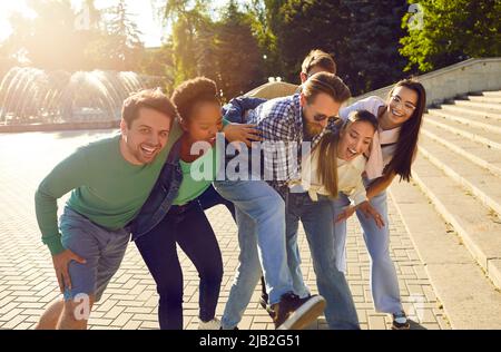 Fröhliche, aufgeregte Männer und Frauen, die am Sommertag im Freien spazieren, umarmen, reden und lachen. Stockfoto