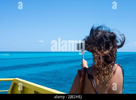 Eine unkenntliche Frau nimmt mit einem Smartphone von einer Fähre im Karibischen Meer, Mexiko, ein Video auf. Stockfoto