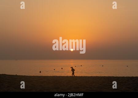 Silhouette eines einstehenden Joggers, der während des Sonnenaufgangs an einem leeren Strand trainiert. Fitness und gesundes Lifestyle-Konzept. Stockfoto