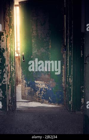 Die schmutzige Tür im Eingang ist offen. In einem dunklen Raum leuchtet das Licht in der Tür. Abstrakter Innenraum aus dunkel lackiertem Beton. Hochwertige Fotos Stockfoto