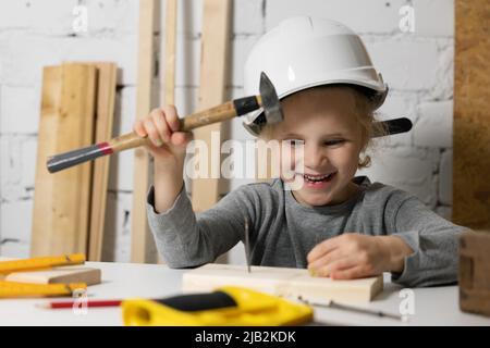 Glückliches kleines Mädchen mit Helm versuchen, einen Nagel in der Werkstatt Hammer. Handwerk Bildung Stockfoto