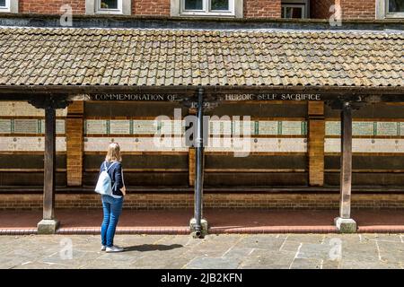 Eine Frau betrachtet Keramiktabletten im Watts Memorial to Heroic Self-Sacrifice im Postman’s Park, London, EC1 Stockfoto