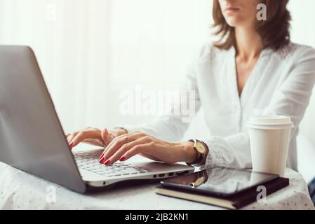 Freiberufliche Mitarbeiterin, Studentin oder Bloggerin, die am Computer am Holztisch im Heimbüro tippt Stockfoto