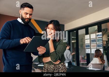 Glückliche Geschäftskollegen, die ein digitales Tablet in einem Sitzungssaal nutzen. Zwei junge Geschäftsleute, die während eines Meetings ein Gespräch führen. Diverse Unternehmer Stockfoto