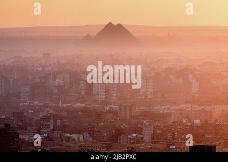 Ägypten, Kairo. Überblick über Kairo bei Sonnenuntergang mit einer der Pyramiden von Gizeh im Hintergrund. Stockfoto