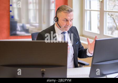 Entschlossener Geschäftsmann bei einem Telefongespräch im Büro, der mit seiner Hand auf seinem Computerbildschirm gestikuliert Stockfoto