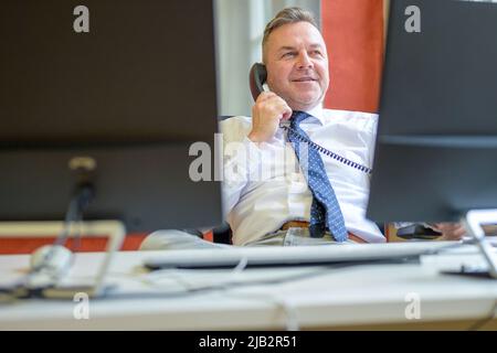 Selbstbewusster Geschäftsmann, der in einem Büro am Telefon spricht, während er sich entspannt, zurückgeschlupft auf seinem Stuhl sitzend Stockfoto