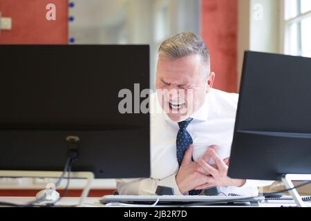 Ein Geschäftsmann, der im Büro einen Herzinfarkt erlitt und sich vor Schmerzen an seiner Brust klammgte Stockfoto