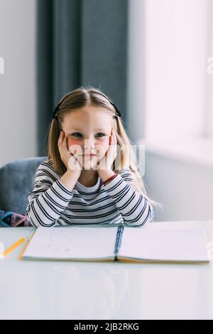 Unglücklich kleines kaukasisches Mädchen Kind sitzen am Tisch zu Hause fühlen faul unmotiviert Hausaufgaben zu machen. Stockfoto