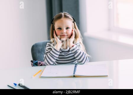 Unglücklich kleines kaukasisches Mädchen Kind sitzen am Tisch zu Hause fühlen faul unmotiviert Hausaufgaben zu machen. Stockfoto