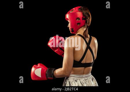 Rückansicht der professionellen Boxerin in Sportschutzausrüstung, die isoliert auf schwarzem Studiohintergrund posiert. Sport, Wettbewerb, Hobby, Ergebnisse Stockfoto