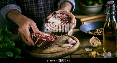 Hoher Winkel der Ernte Mann in kariertem Hemd Putting Hälften von Rotkohl auf Schneidebrett in der Nähe von Knoblauch und Basilikum mit Öl und Walnüssen während gesunde lun Stockfoto