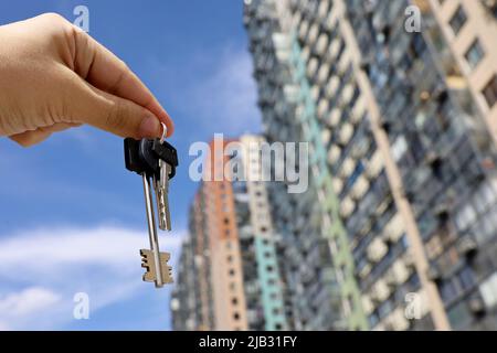 Hausschlüssel in männlicher Hand auf dem Hintergrund neuer Wohngebäude. Immobilienmakler, Umzug oder Vermietung von Immobilien Stockfoto