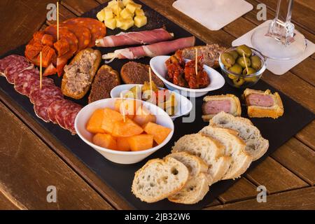 Wurst und Käse auf braunem Hintergrund in Scheiben geschnitten. Italienische Antipasti-Wein-Snacks. Käse, mediterrane Oliven, Prosciutto mit Melone, Brotstangen Stockfoto