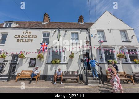 Southend auf See, Großbritannien. Juni 2022. An einem sonnigen Tag versammeln sich die Menschen vor dem Crooked Billet, einem traditionellen britischen Pub in Leigh-on-Sea, Essex. Das weiß gestrichene Gebäude verfügt über hängende Blumenkörbe, Union Jack-Fahnen und Bänke entlang des Bürgersteigs. Die festlichen Dekorationen deuten auf eine nationale Feier oder eine lokale Veranstaltung hin, bei der die Gäste die Atmosphäre unter einem klaren blauen Himmel genießen. Das Crooked Billet in Old Leigh. Szenen rund um Southend on Sea, während die Menschen das Queens Platinum Jubilee und den Feiertag feiern. Penelope Barritt/Alamy Live News Stockfoto