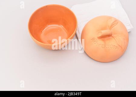 Natürlicher Terrakotta-Topf mit Deckel zum Kochen von Äpfeln von Romertopf mit weißem Cootn-Handtuch auf einem hellen Tisch Stockfoto