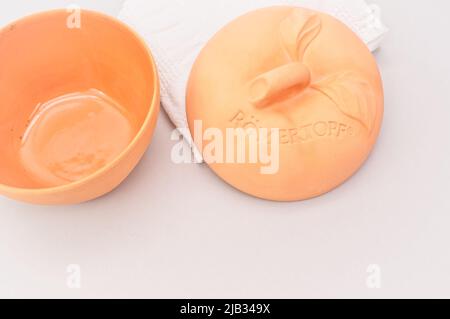 Natürlicher Terrakotta-Topf mit Deckel zum Kochen von Äpfeln von Romertopf mit weißem Cootn-Handtuch auf einem hellen Tisch Stockfoto